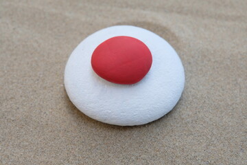 Creative japanese flag concept composed with red and white colored stones on the beach
