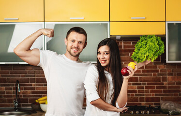Obraz premium Happy friends preparing food for dinner, posing in the kitchen holding vegetables and fruits. Promoting healthy eating