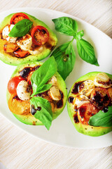 Healthy food. Avacado with cherry tomatoes, mozzarella cheese, basil under pesto sauce with balsamic vinegar. High key. Selective focus. Vegetarian food.