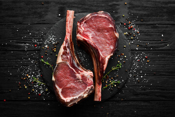 Dry aged raw tomahawk beef steak with spices. On a black wooden background. Top view. Free copy...
