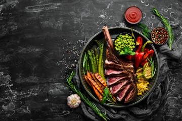 Grilled steak on the bone with grilled vegetables. On a black background. Top view. Free copy space.