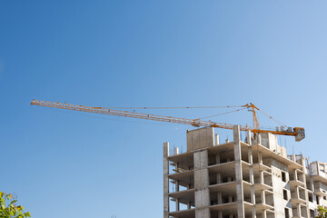 Fototapeta na wymiar Construction tower crane against the blue sky. Concept of development of the architectural appearance of the city. Construction of multi-family residential buildings. Monolithic concrete works.