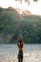 Rear view of young fit and sporty woman in sportswear stretching before the workout on the wooden pier on the lake near the green forest. Active concept. Copy space