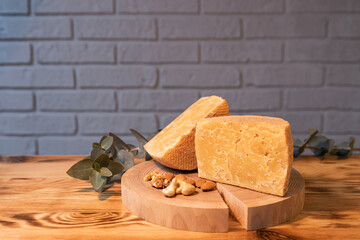 A head of aged cheese cut in half on a wooden Board with various nuts on the background of a brick wall