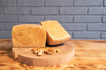 A head of aged cheese cut in half on a wooden Board with various nuts on the background of a brick wall