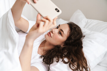 Obraz na płótnie Canvas Photo of attractive woman taking selfie on cellphone while lying on bed