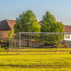 Square crop Soccer goal on vast green grassy field in front of houses viewed on a sunny day