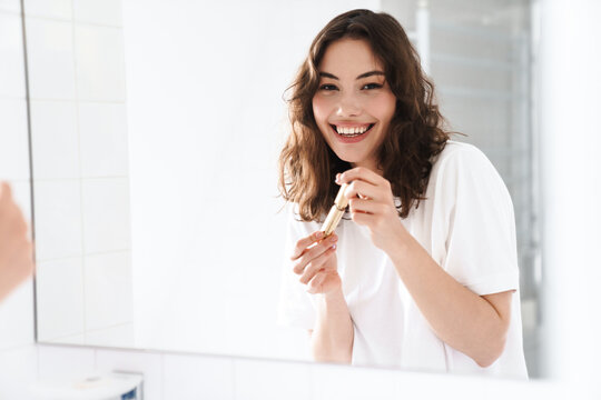 Photo of woman smiling and holding mascara while looking at mirror