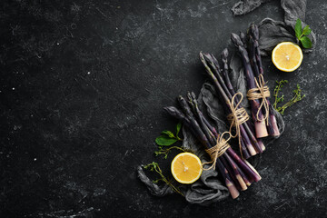 Fresh purple asparagus with lemon on a black stone background. Healthy food. Top view, free copy space.