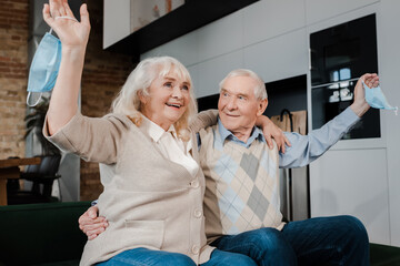 cheerful senior couple holding medical masks on sofa after self isolation