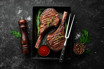 Juicy steak grilled on the bone with spices and herbs. On a black stone background. Top view. Free...