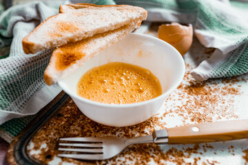 Whipped with a fork and mixed raw egg broken into a white bowl with yolk and protein, next to the shell, fork and towel on a rusty metal background as at home in the village, everything simple and ord