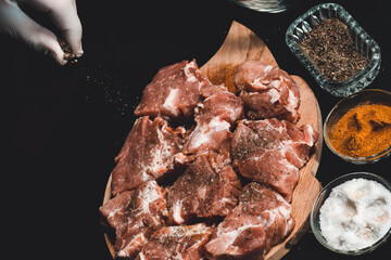 The chef of the restaurant sprinkles with curry spices and basil meat on a black background. Marinating pork for barbecue and ham.