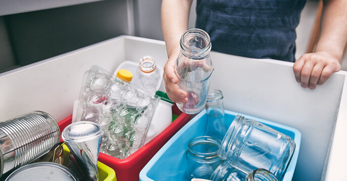 The boy is throwing the  garbage to the one of four different bin for sorting trash.