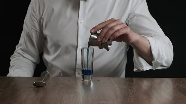 Bartender pouring blue curacao liquor into glass from jigger