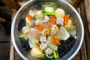Clear soup with tofu, minced pork and various vegetables in a metal pot.