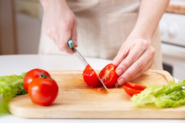 Wooden Cutting Board with Fresh Herbs, Lettuce and Raw Vegetables on Rustic Wood Board. Cooking background. Female Hands cut with a knife Juicy red tomato. Ingredients for salad