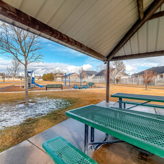 Square Green metal tables and benches inside a pavilion with melted snow on a sunny day