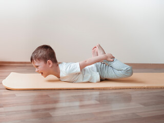 Young boy doing yoga basic posture Dhanurasana, Bow Pose, at home. Sport at home for kids