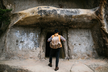 A young male traveler explores the ruins of a cave city in the mountains. Active tourism