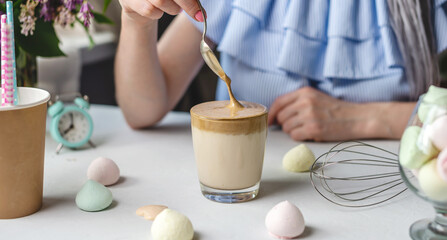Woman is picking up a spoon and gently stirs the thick whipped mousse in a glass of cold coffee. Gentle atmosphere and sunny beautiful summer morning