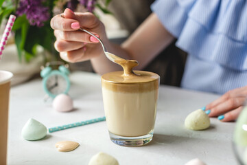 Woman is picking up a spoon and gently stirs the thick whipped mousse in a glass of cold coffee. Gentle atmosphere and sunny beautiful summer morning