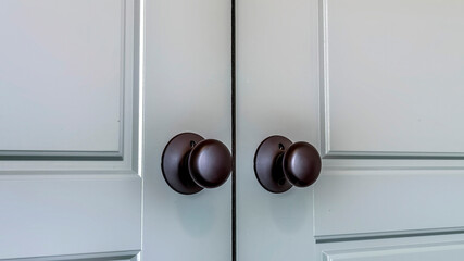 Panorama crop Matte black round door knobs of a double door with paneling inside a home