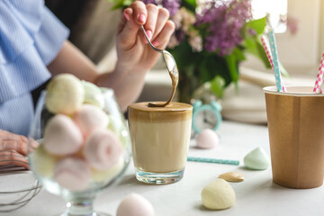 Woman is picking up a spoon and gently stirs the thick whipped mousse in a glass of cold coffee. Gentle atmosphere and sunny beautiful summer morning