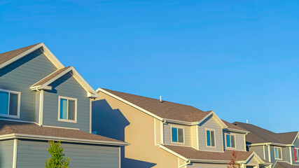 Panorama frame Homes with horizontal wall sidings and front gable roofs againts clear blue sky