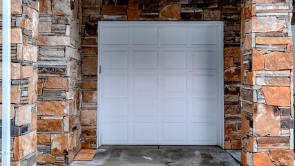 Panorama crop White panelled garage door of home with gray siding and stone exterior wall