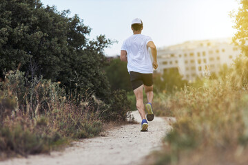 Back view of fit athlete man running in park with a hat and lens flare