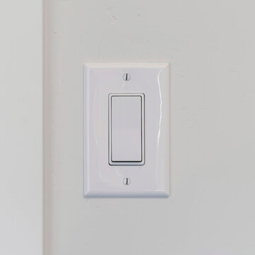Square Electrical rocker light switch on white wall against blurry door background