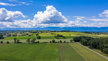 Fototapeta na wymiar Aerial drone shot of the countryside and farm land around the area of Geneva, Switzerland. The large white clouds and blue sky and green fields of this picturesque landscape.