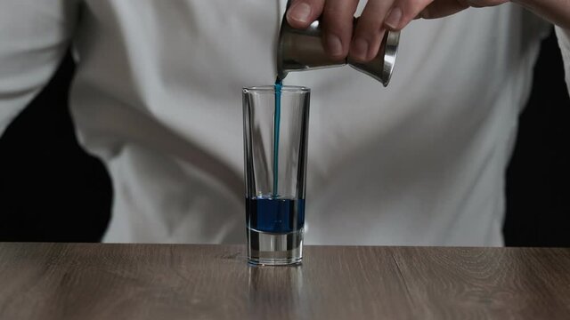 Bartender pouring blue curacao liquor into glass from jigger. Close up
