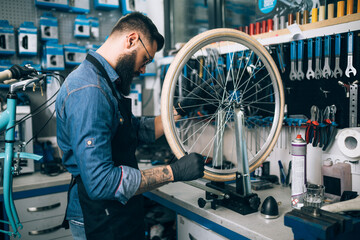 Young beard bicycle mechanic repairing bicycles in a workshop..