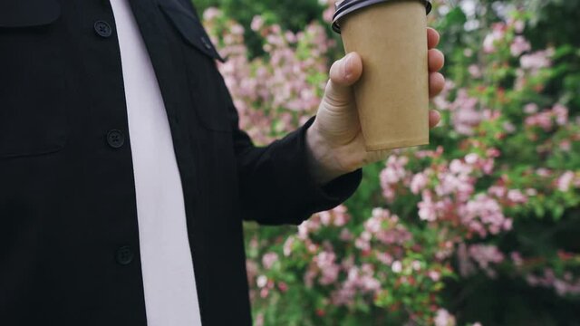 Man holds coffee on the background of beautiful flowers in the park