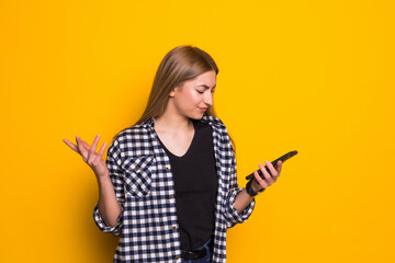 Angry young woman says irritated cell phone to hear bad news via the phone. Portrait of a girl with a mobile phone, on a yellow background