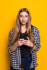 Photo of cheerful cute beautiful young woman chatting by mobile phone isolated over yellow background.