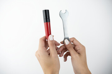 woman's hands holding lip gloss in one hand and wrench in another on isolated white background, beauty industry versus car repair