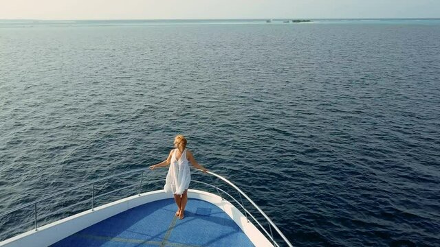 Beautiful adult woman in flowing white dress stand on deck of luxurious expensive yacht. Vacation or holiday goer tourist enjoy pacific ocean on rich people retreat, white cruise boat with deck pool 