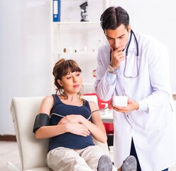 Obraz premium Young doctor checking pregnant woman's blood pressure