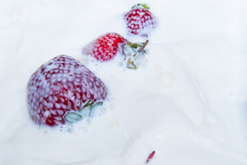 Obraz na płótnie Canvas Strawberries falling into milk, spray, close up