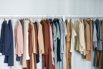 Clothes hanging on rail in modern closet or in a small shop, showroom. Colors of fall and summer.