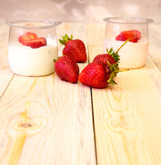 Sliced ​​strawberries in half, jars of yogurt on a wooden table