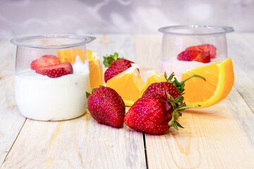 Sliced ​​strawberries in half, orange sliced ​​jars of yogurt on a wooden table