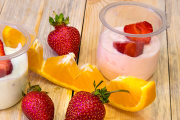 Sliced ​​strawberries in half, orange sliced ​​jars of yogurt on a wooden table