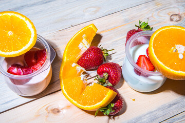 Sliced ​​strawberries in half, orange sliced ​​jars of yogurt on a wooden table
