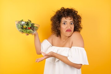 Beautiful European girl pointing aside with both hands showing something strange and saying: I don't know what is this. Standing against gray background. Advertisement concept.