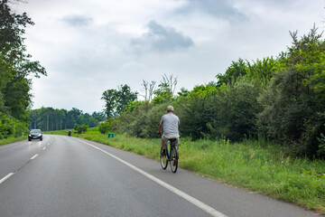 Gray haired man riding bicycle on bike lane on edge of road