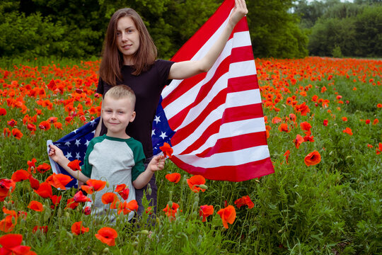woman and boy stand wrapped in american flag in the middle of a field of red flowers. Concept of Memorial day and Honor . High quality photo